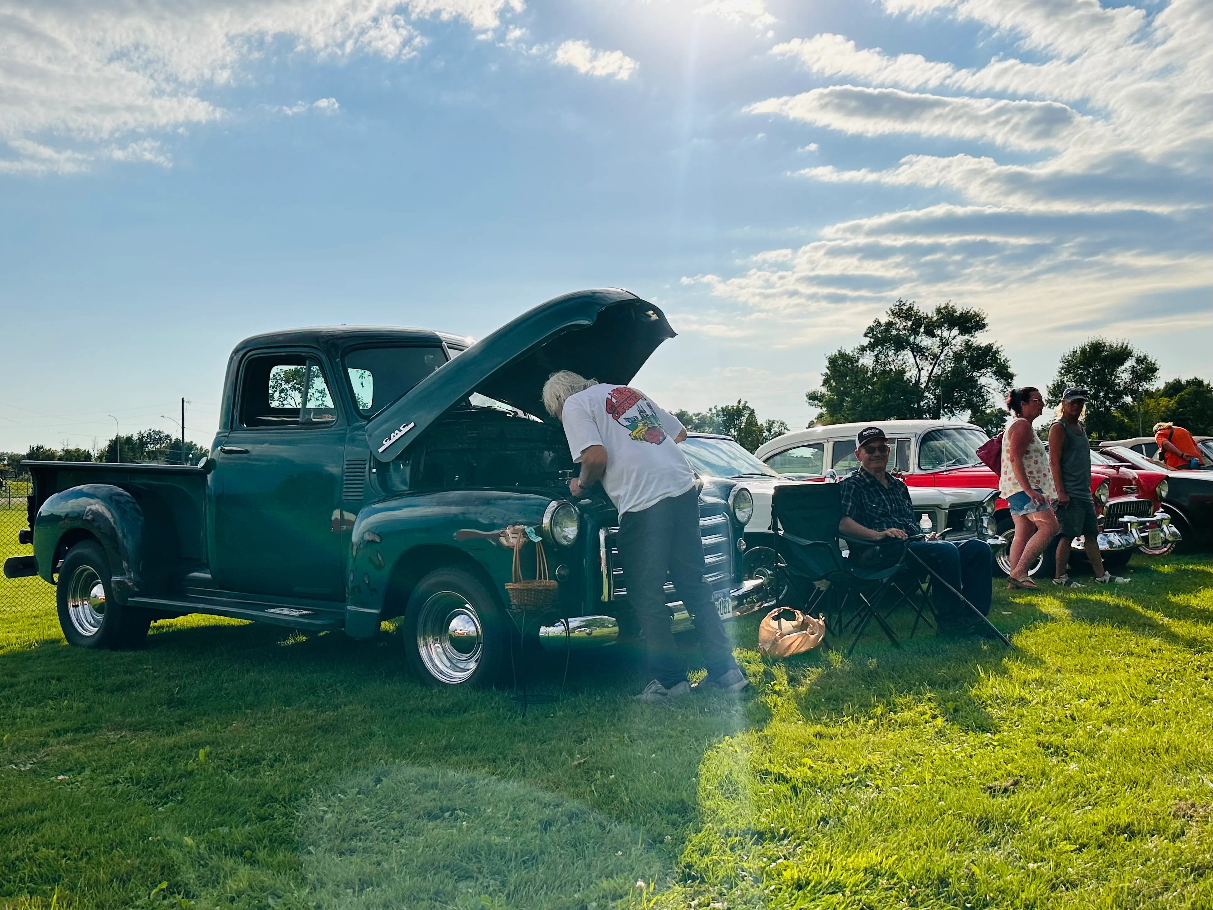 Vintage teal pickup truck with hood open as attendees admire it