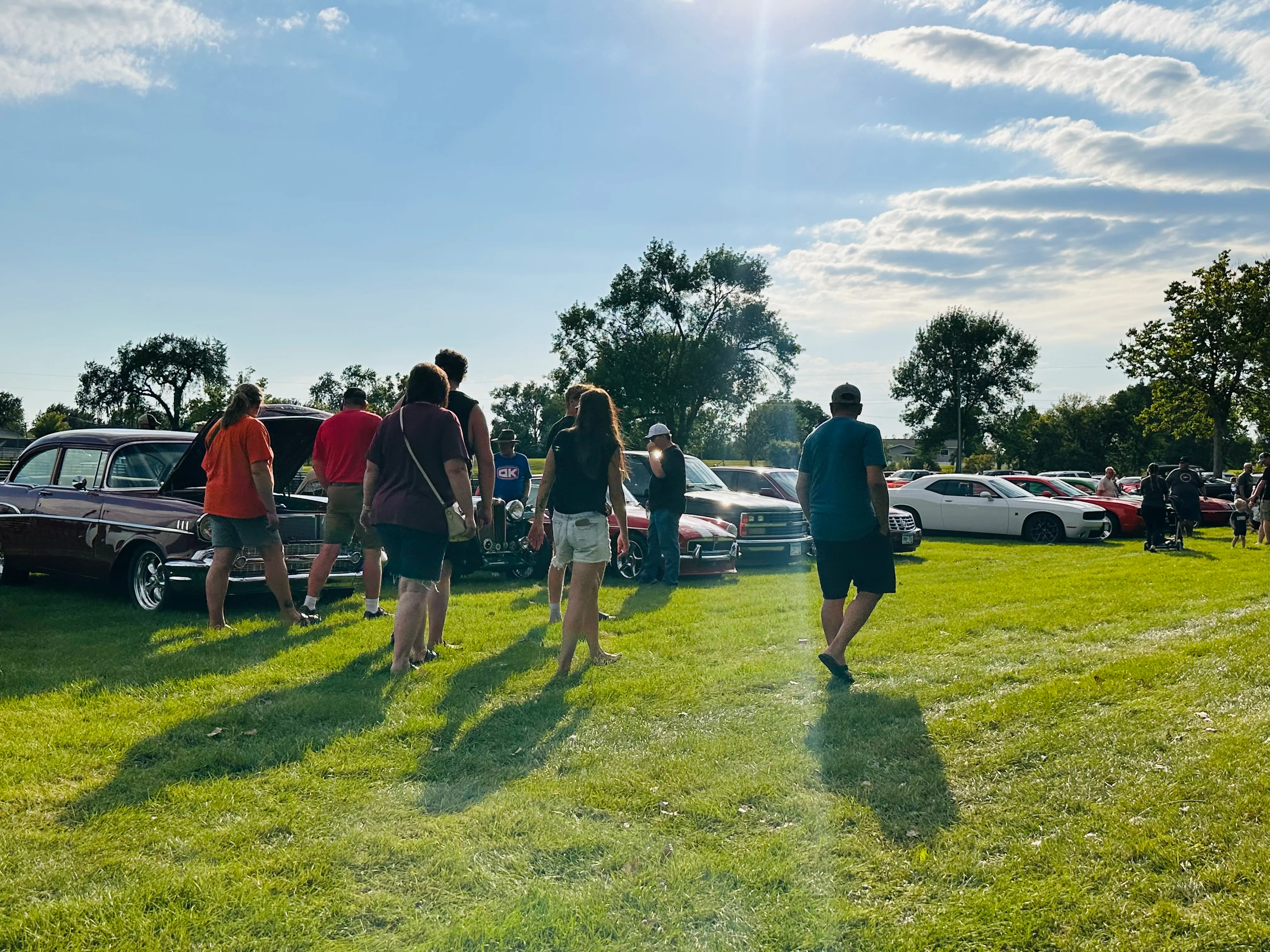 Wide shot of attendees walking between classic cars on the grass field