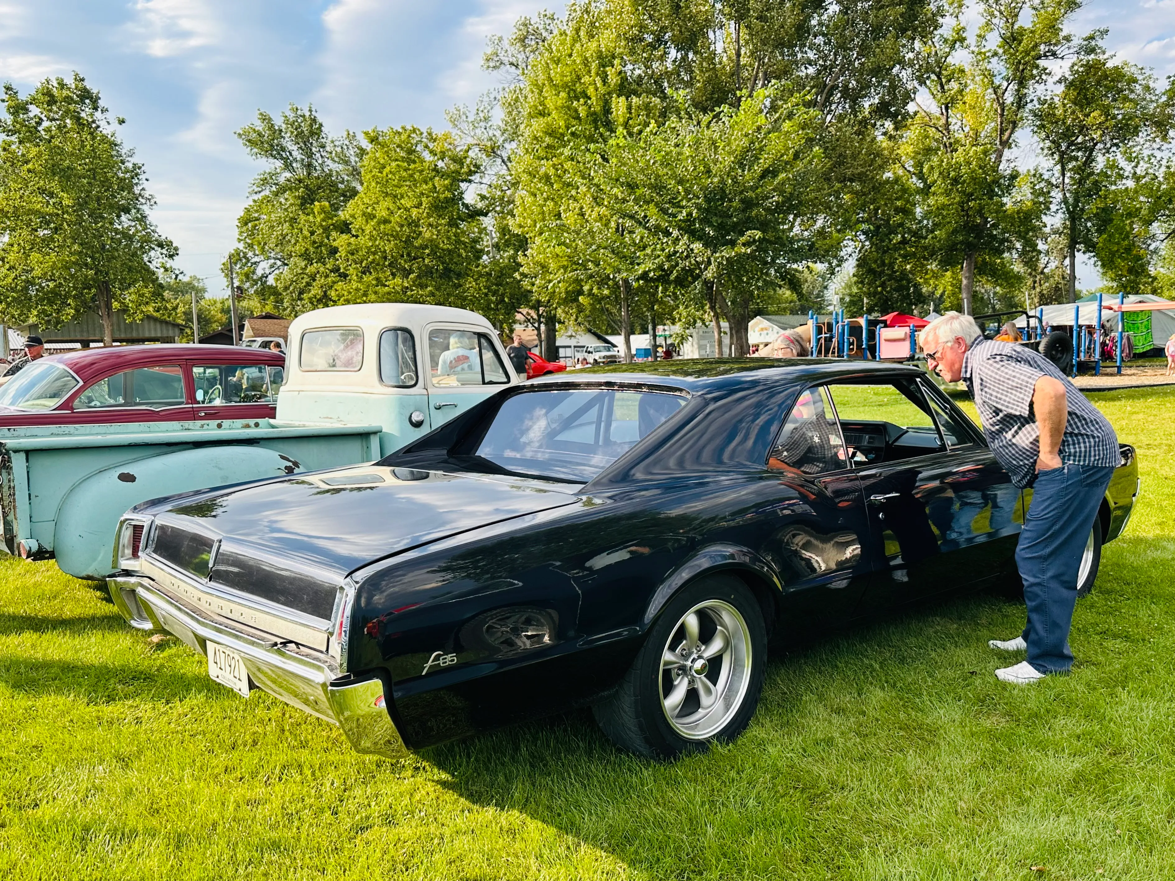 Two men examining a black muscle car next to a cream vintage car