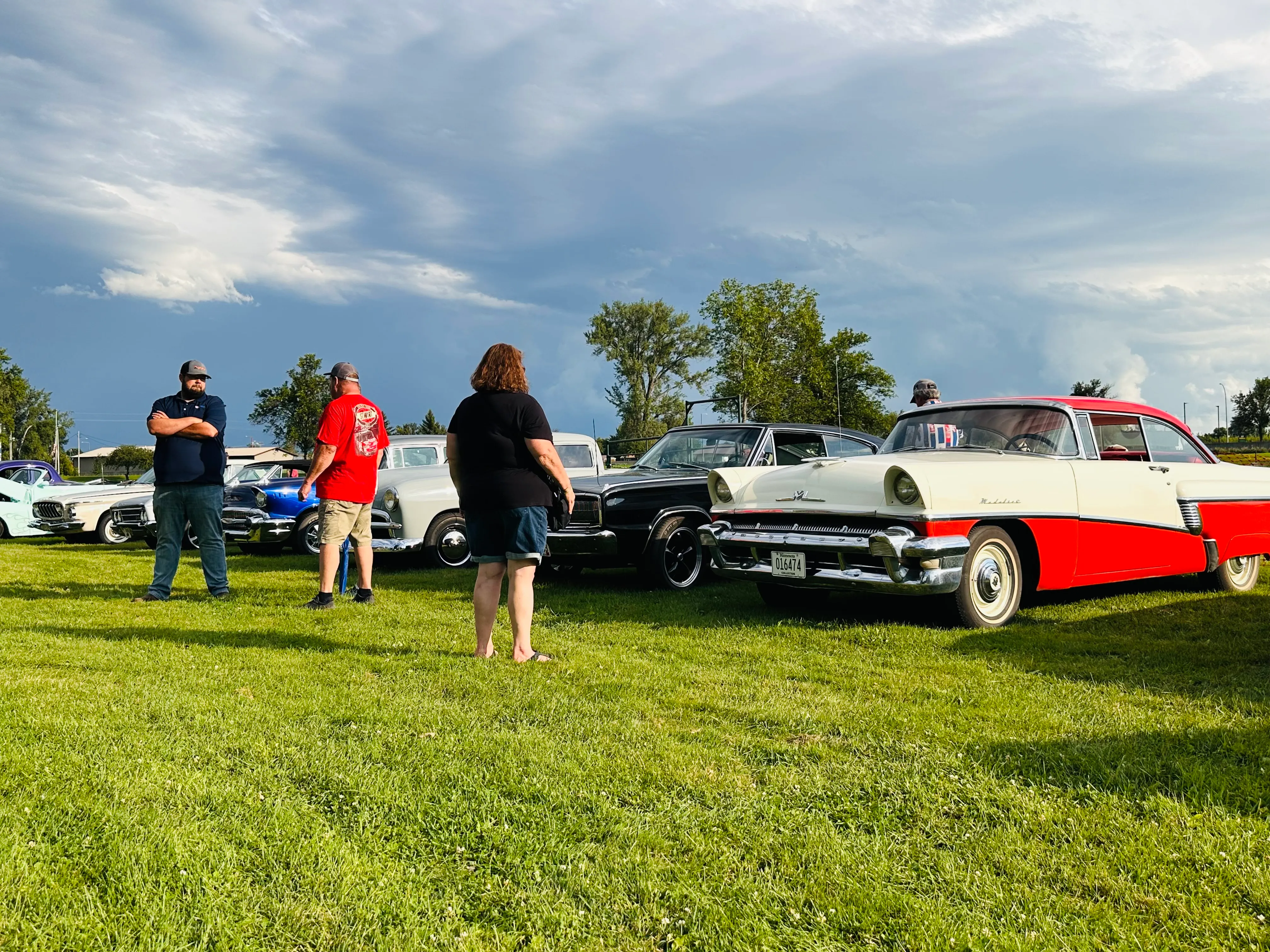 Large group of attendees gathered around classic vehicles with carnival games in background